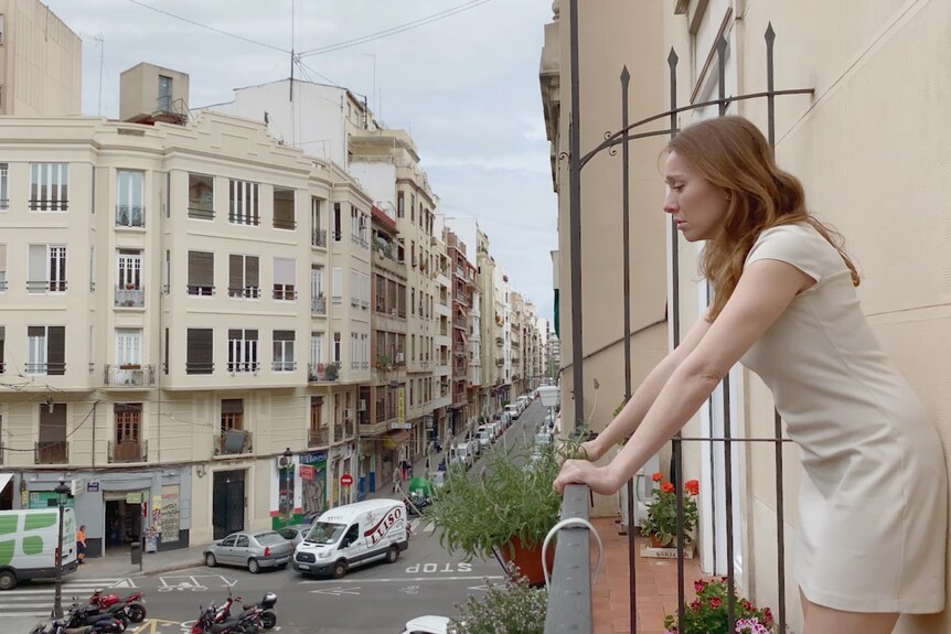 A scene from web series Cancelled with a woman standing on a balcony overlooking a street in Valencia, Spain