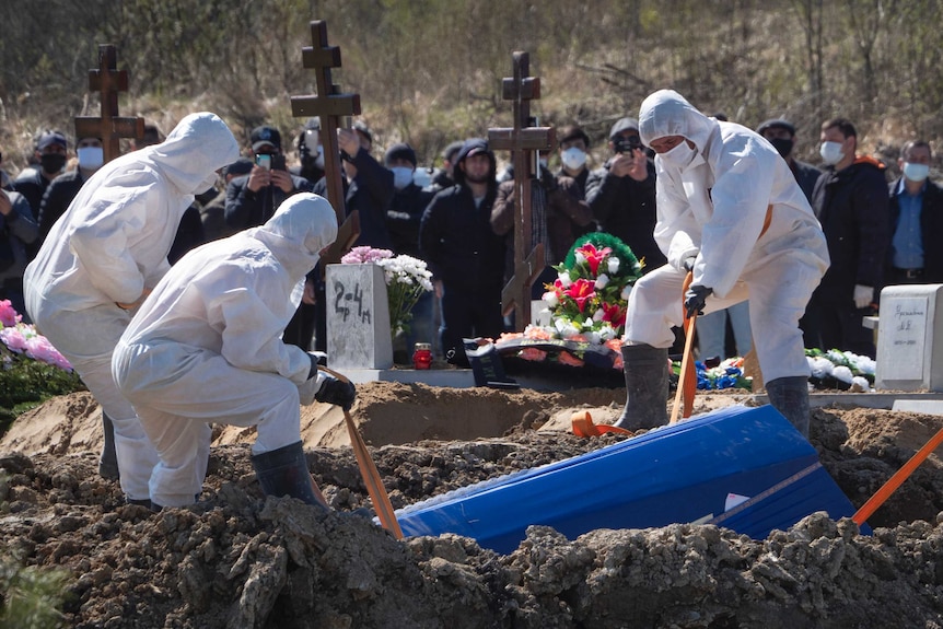 Grave diggers wearing protective suits bury a COVID-19 victim.