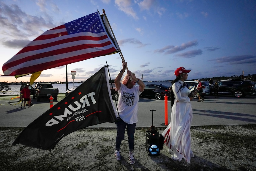 Two women fly an American flag and a Trump flag in a carpark 