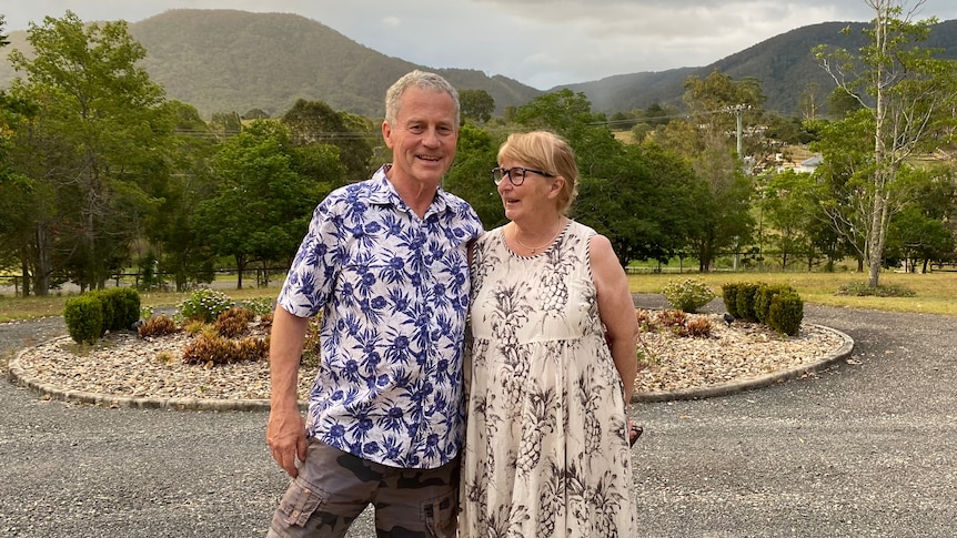 A man and woman stand smiling in front of a mountain range 