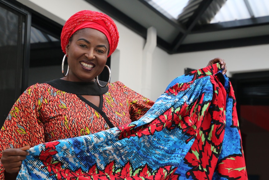 Safuratu Bakare wearing a bright red hat and holding up a bright fabric