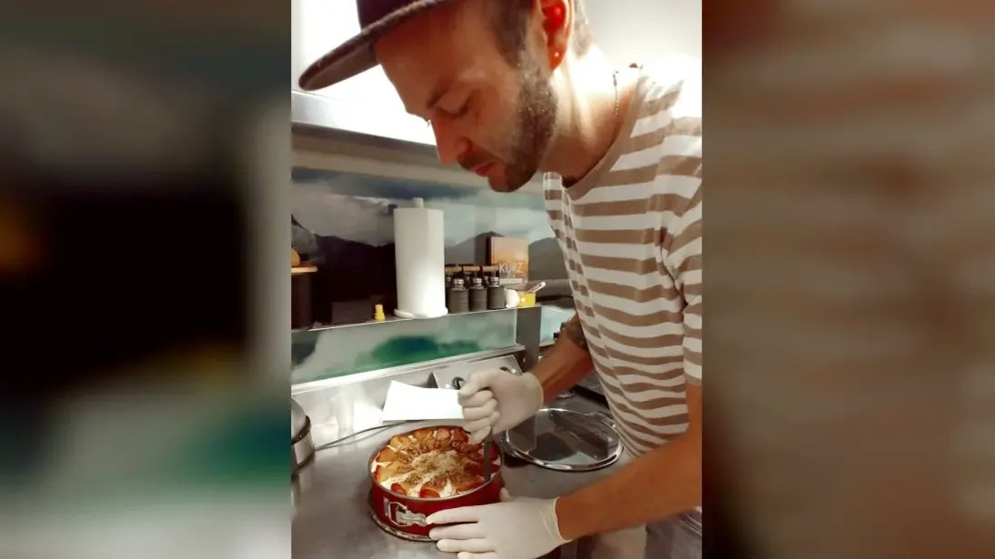 一位留着短胡子的年轻男子在商业厨房里切蛋糕。