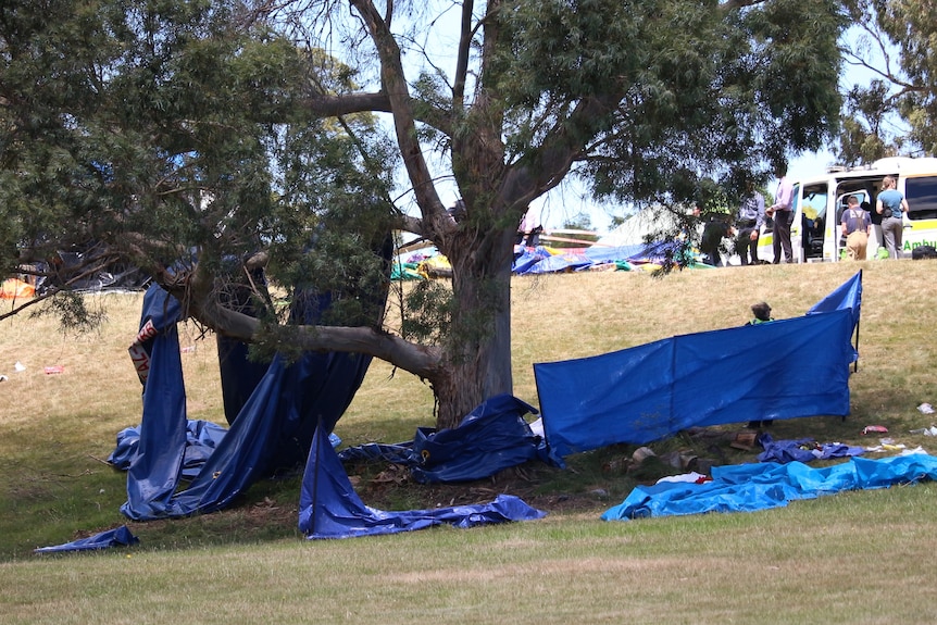 Blue plastic hangs from a tree with debris scattered below it.