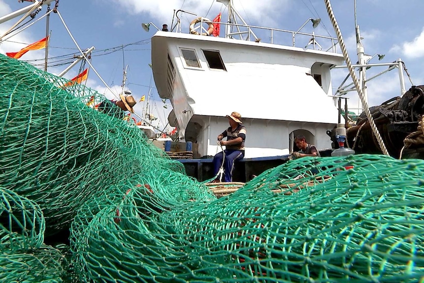 Captain Lin Jianchang mends nets on his trawler. Captain Lin Jianchang mends nets on his trawler.