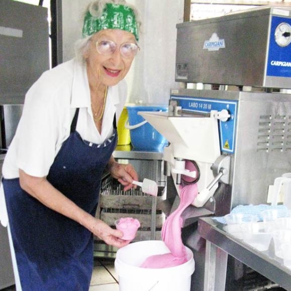 An 89yo woman pouring a pink ice cream into a bucket.