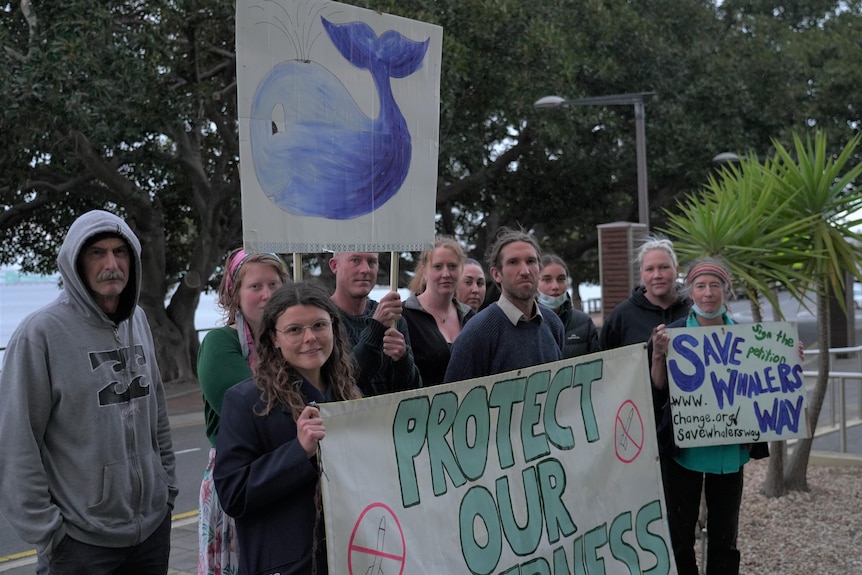 A group of protesters stand outside with concerned looks and signs