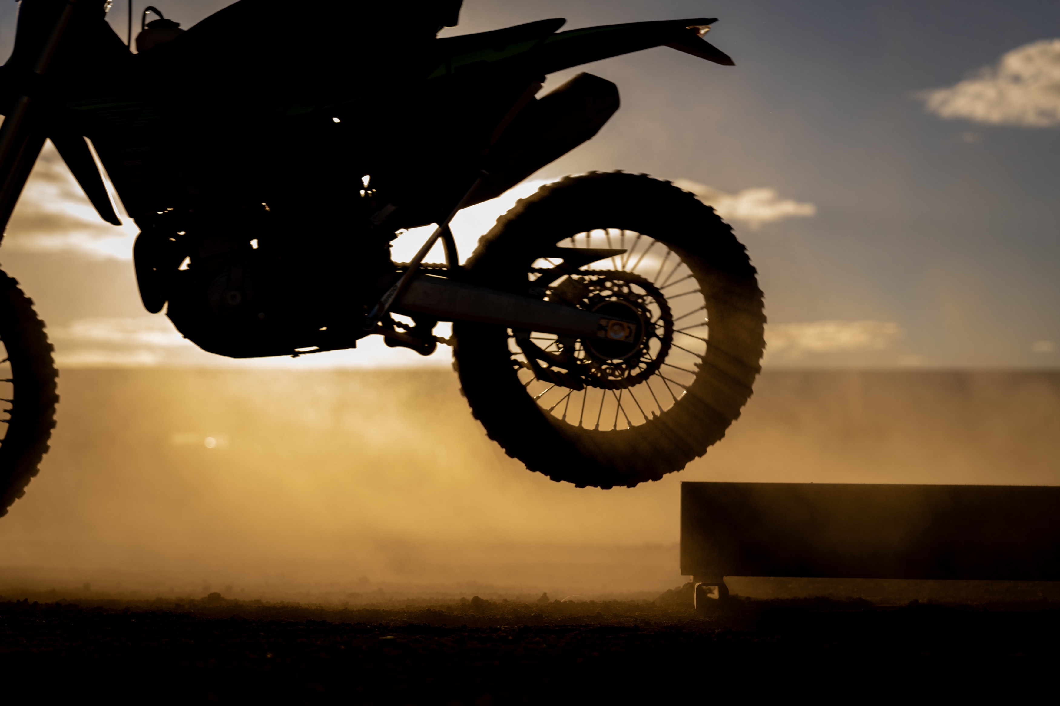 A sillouhette of a motorbike wheel coming off a platform with dust around