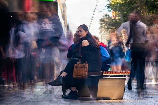 Woman sits on a bench in Rundle Mall as blurred shoppers walk past.