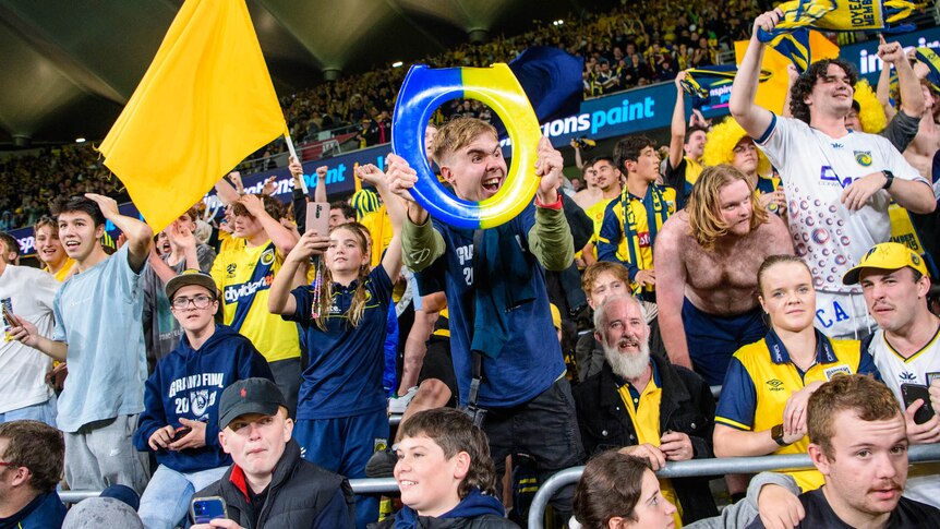 Central Coast Mariners fans celebrate, one holding a blue and yellow toilet seat