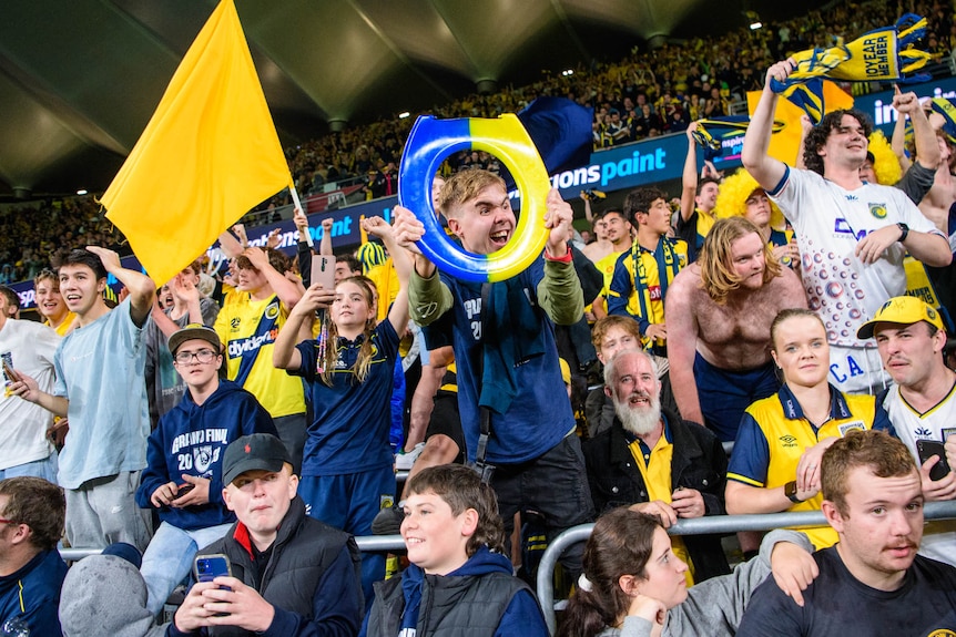 Central Coast Mariners fans celebrate, one holding a blue and yellow toilet seat