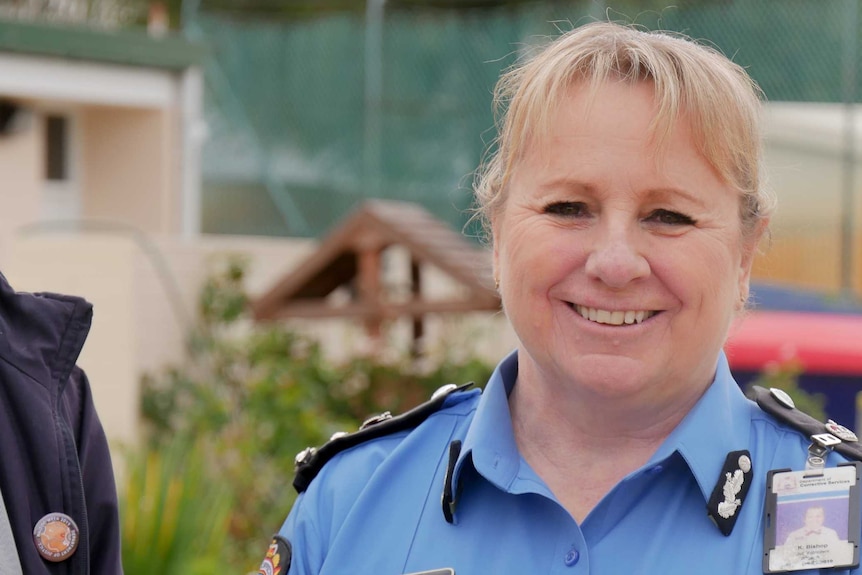 A female prison officer in blue uniform looks directly at the camera. 