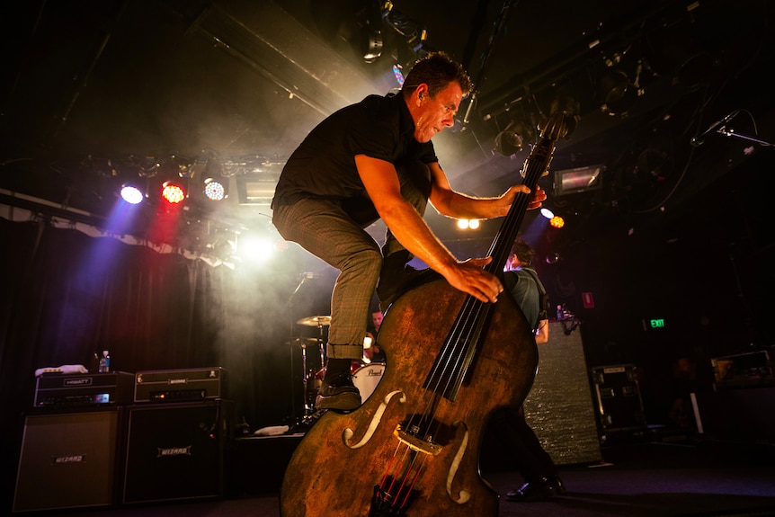 A man balances on top of a double bass he is playing on a stage