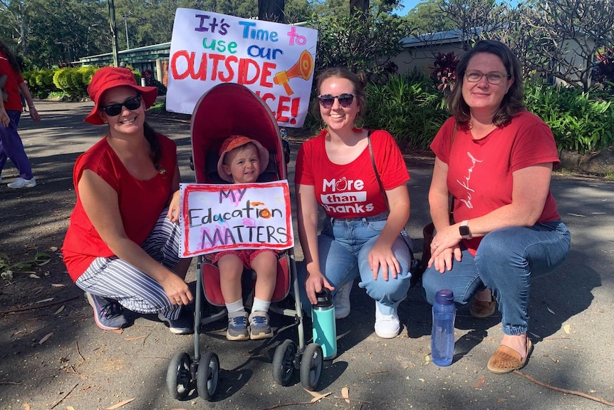 Three adults kneel next to a baby in a pram