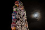 A near-full moon shines next to the Ferris Wheel.