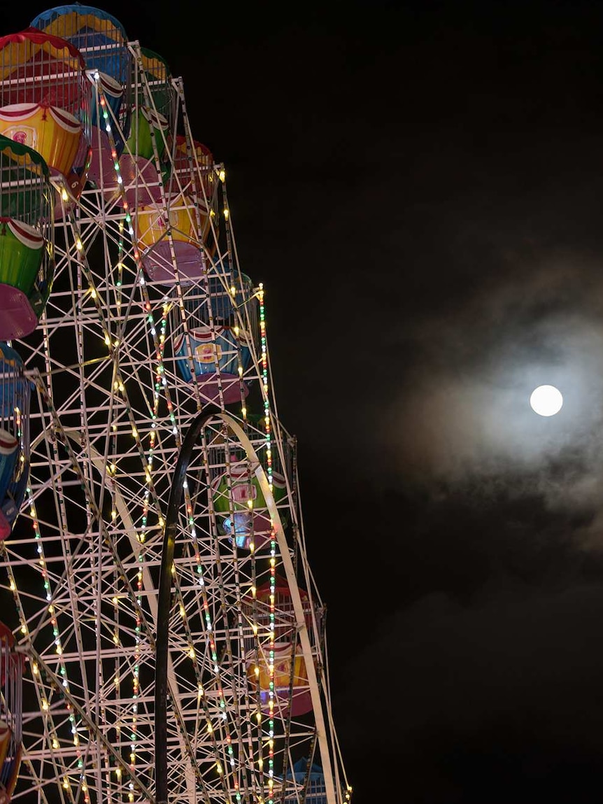 A near-full moon shines next to the Ferris Wheel.