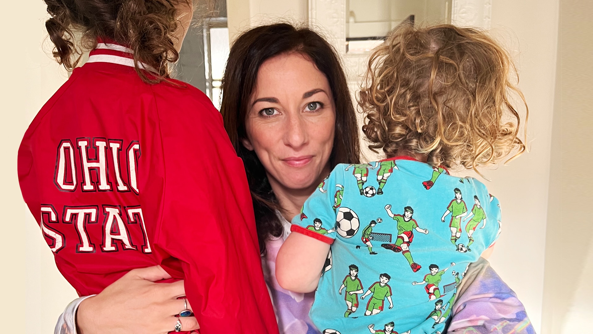 a womanw ith dark long hair is hugging two children with their back to the camera