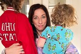 a womanw ith dark long hair is hugging two children with their back to the camera