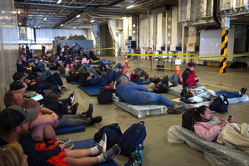 Evacuees rest on the ground of the New Zealand naval ship HMNZS Canterbury.