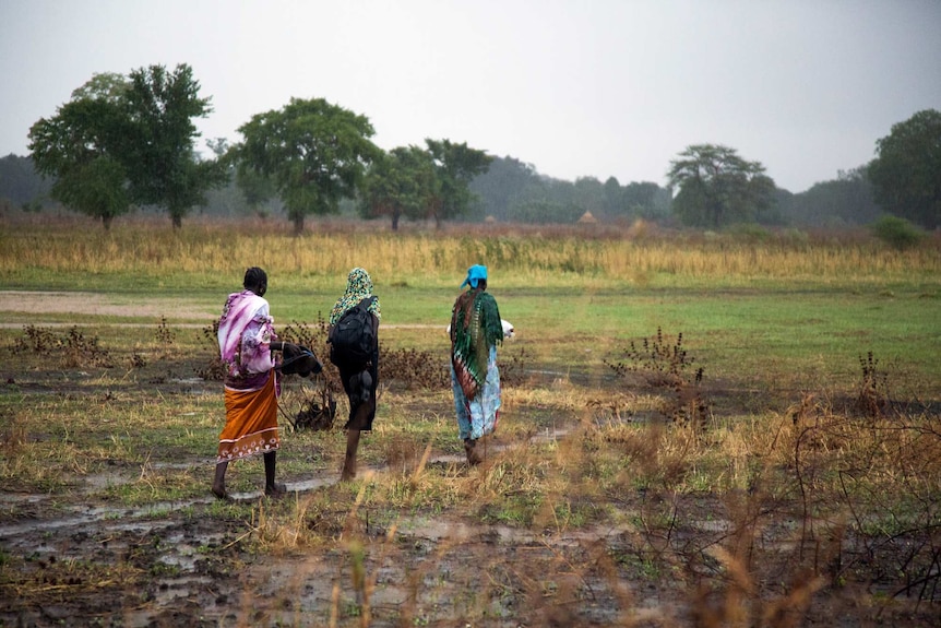 Nyamuoch, in black, walks with her aunt and another relative to her mud and straw home in the distance.