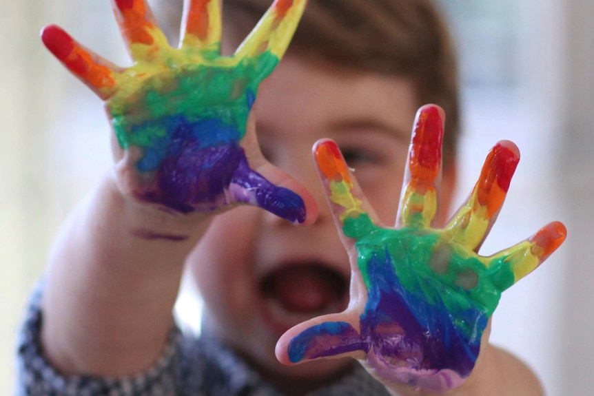 Britain's Prince Louis smiles for the camera with bright paint on his hands.
