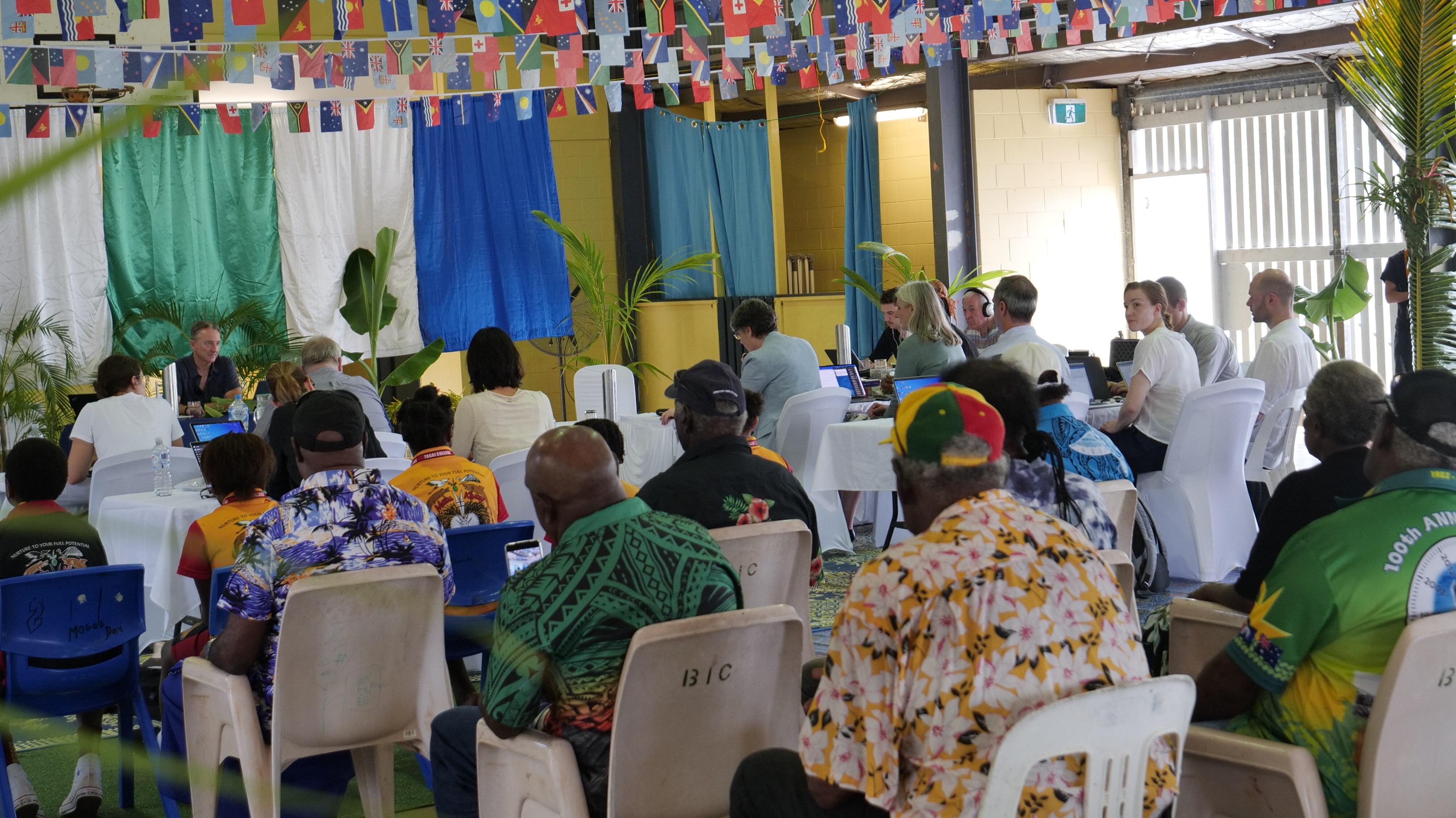 People sitting in chairs at a community hall for a formal hearing