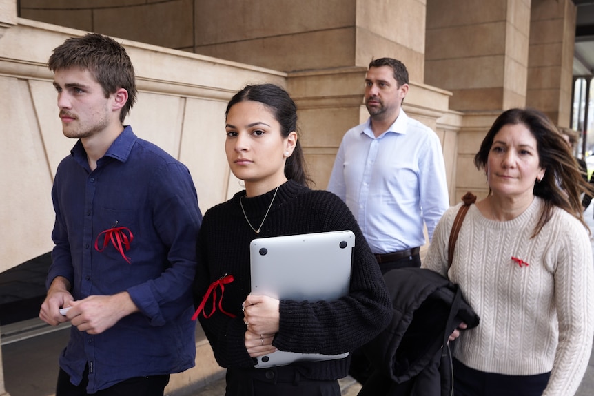 Four people wearing red ribbons walk outside a court building