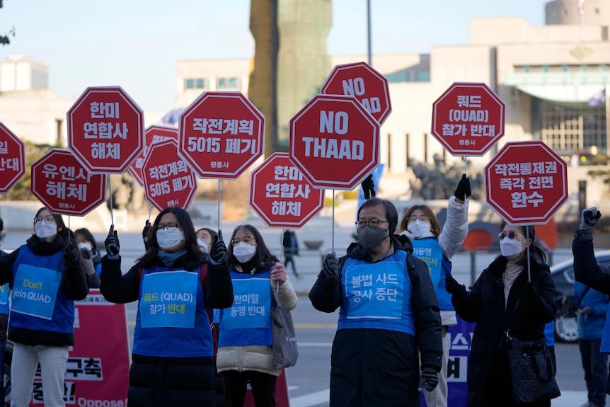 A group of people wearing blue vests hold red stop sign placards during a rally against nuclear weapons in south korea 
