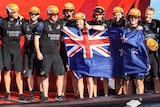 Team New Zealand crew members stand with the New Zealand flag as they celebrate winning the America's Cup.