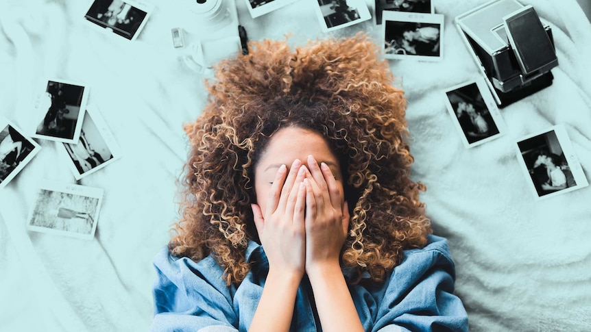 A young woman lying on a bed covers her eyes with her hands.