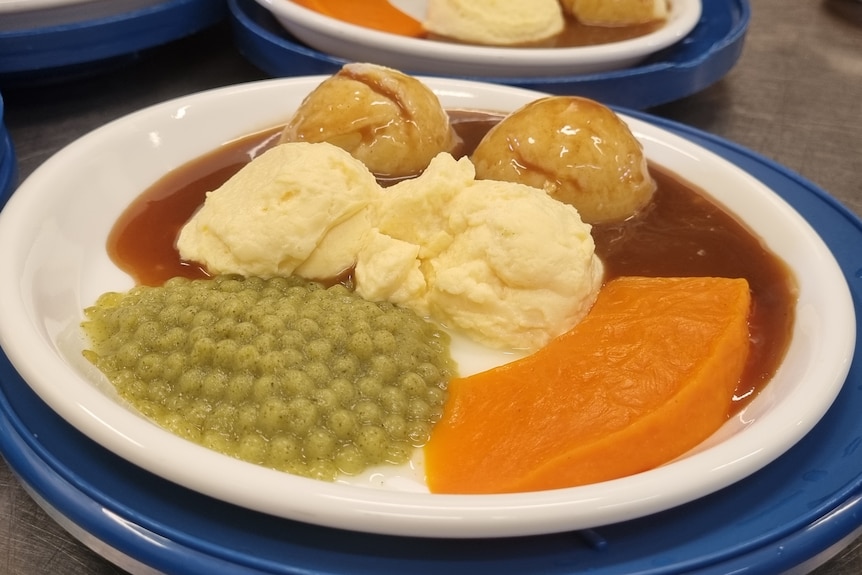 A plate of peas, mashed potato, pumpkin and gravy on a plate.