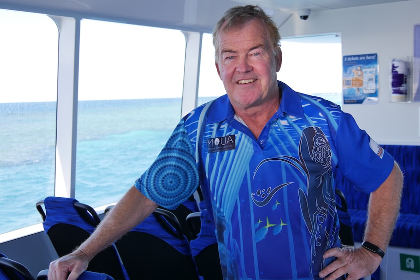 A smiling man in a blue shirt inside a ferry with the ocean in the background