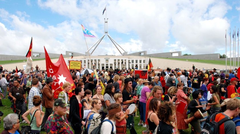 Thousands of people march across the front of Parliament House protesting against the