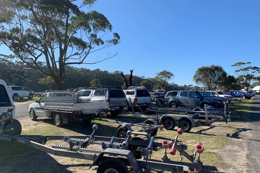 A carpark near a lake with many four-wheel drives and boats parked in it.