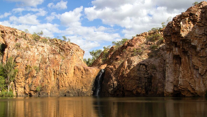 a waterfall on sandstone cliffs flowing into a large natural pool.
