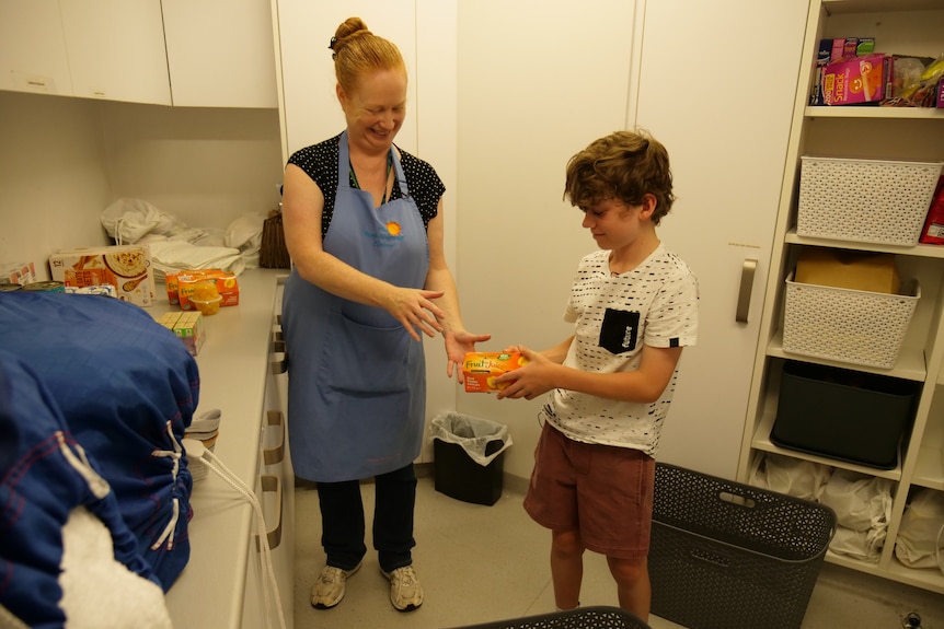 A young boy hands a box of food to a woman