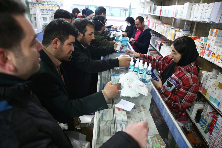 People lining up at a pharmacy counter buying hand sanitizer and face masks
