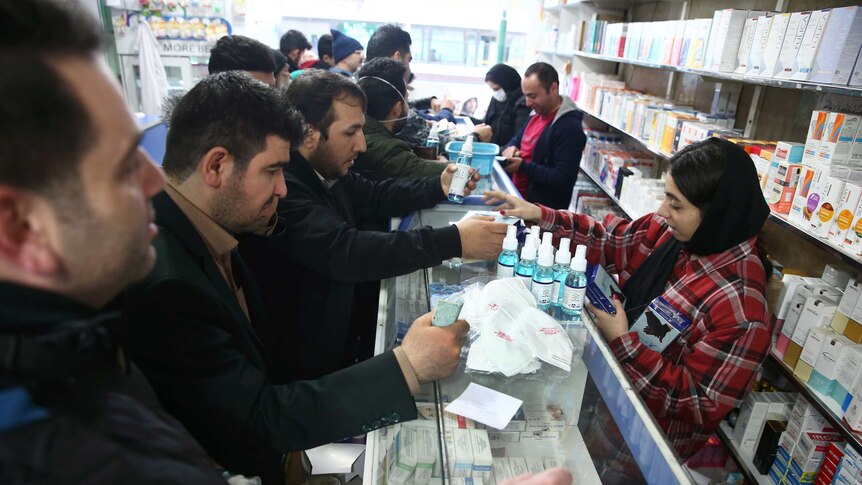 People lining up at a pharmacy counter buying hand sanitizer and face masks