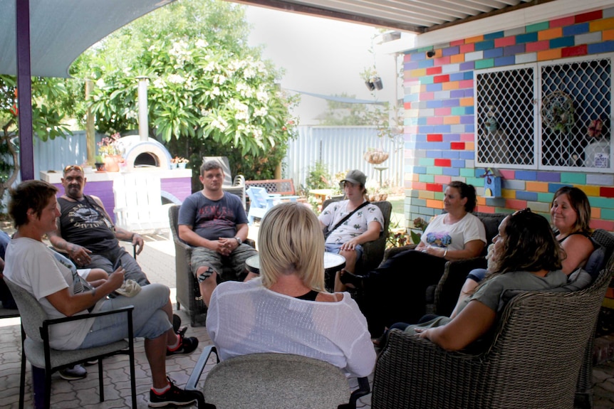 A group of people sitting around outside a brightly coloured building in a circle