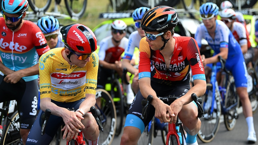 Two professional cyclists on bicycles talk amid a crowd of cyclists.