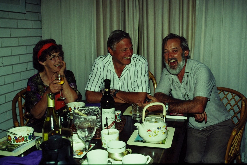 Two men and a woman sit at a table together laughing.