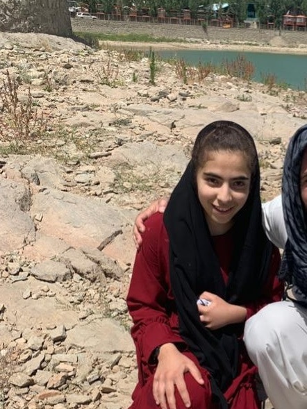 A girl in black hijab smiling with rock in the background. 