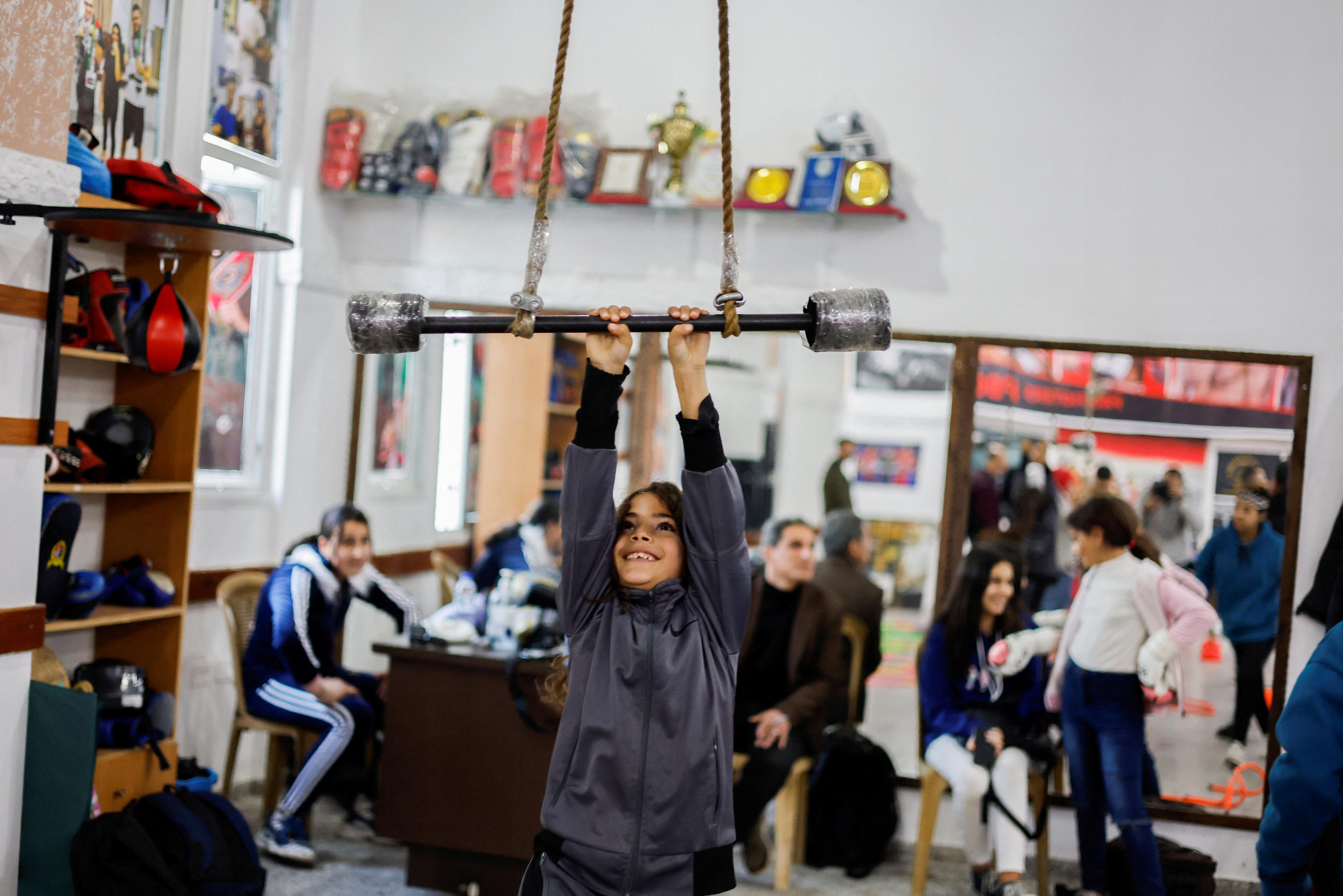 A young girl smiles as she holds on o a horizontal bar attached to rope. 