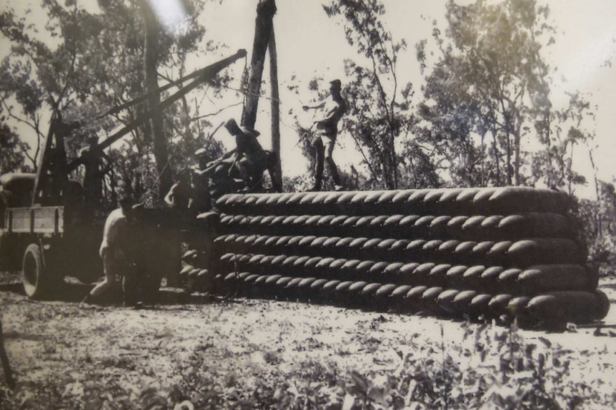 An archival black and white photo of soldiers loading bombs with a crane