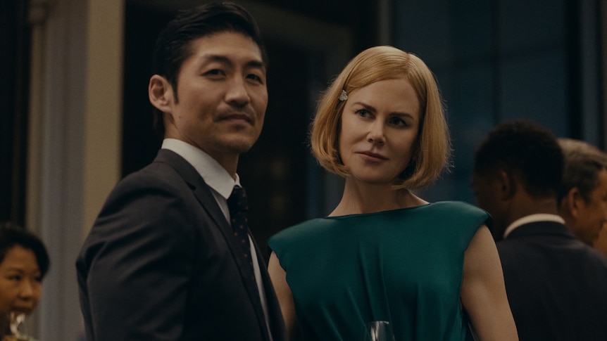 A TV still of Brian Tee and Nicole Kidman, standing together, dressed in formalwear, at a party.