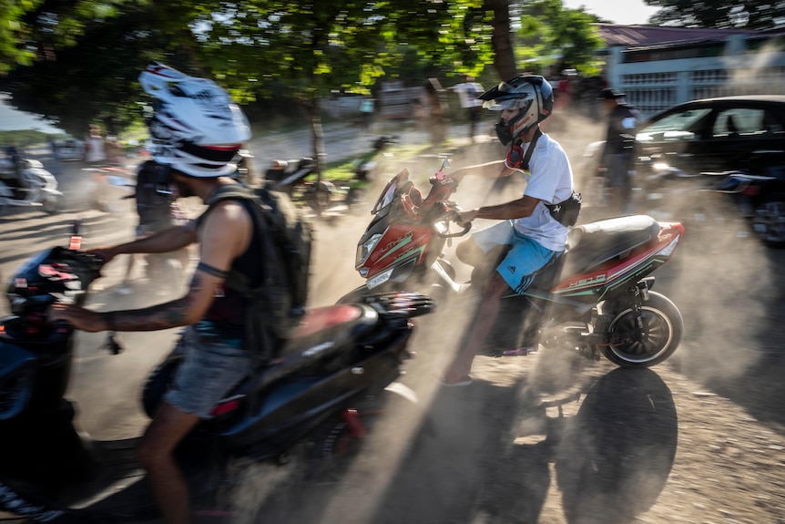 People on e-scooters wearing motorbike helmets drive through smoke/dust cloud