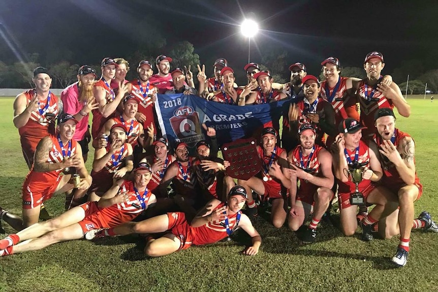 A team of football players wearing red holds up a 2018 premiership flag