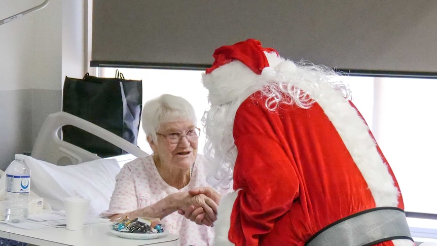 An elderly woman accepts a present from Santa in hospital.