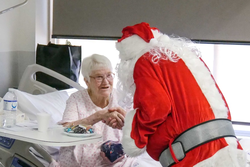 An elderly woman accepts a present from Santa in hospital.