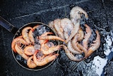 Pans of tiger and king prawns on a barbecue