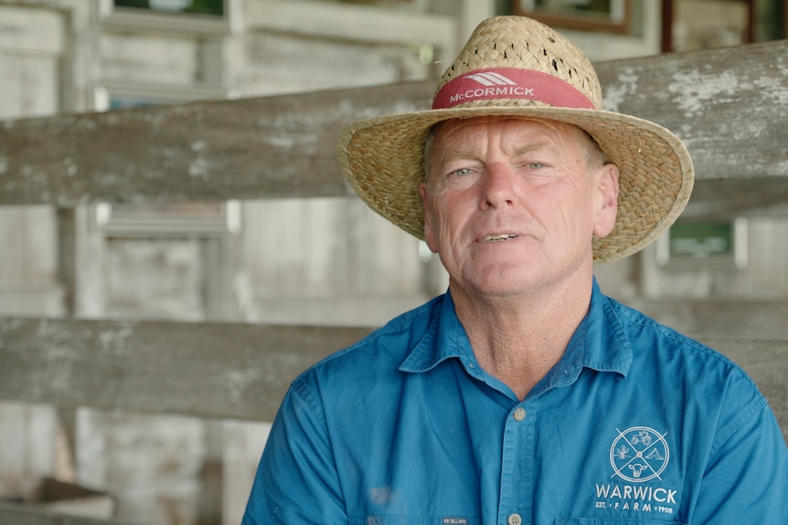 Un homme regarde la caméra, c'est un agriculteur portant un chapeau et se tient dans un ancien hangar de traite